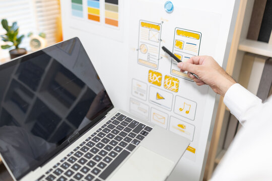 
Person sketches digital interface on paper, pens poised. Laptop sits open, ready for work. Cards and wireframes lie scattered nearby. Focused expression, calm, intent. Ideal for UX design, planning

