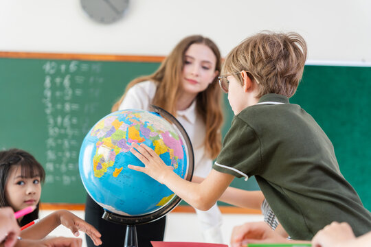 Young students learning world geography, school boy pointing at globe in class, Education concept, diverse children and teacher exploring the world map on a globe in the classroom