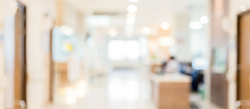 A blurred interior view of a modern healthcare facility, featuring well-lit hallways and a reception area with people in the background, creating a sense of activity.