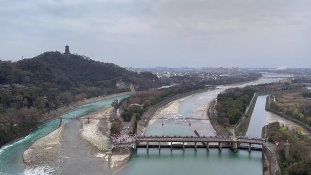 A historic water diversion project with a dam, split rivers, and forested mountains under an overcast sky.