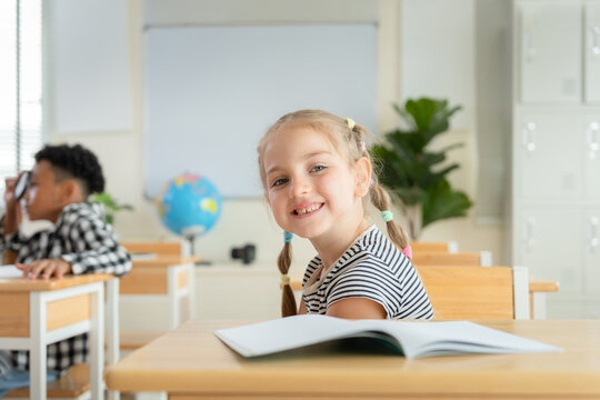 Portrait of Smiling young girl sitting at classroom desk with notebook, Cute primary student studying in school, Happy elementary school girl smiling at desk in classroom