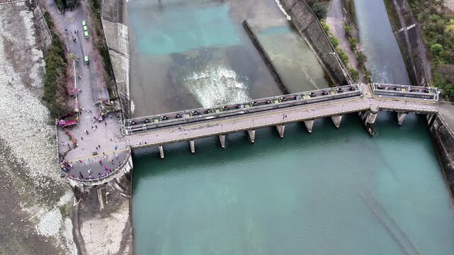 Aerial shot of a concrete water control dam with sluice gates, showing water flow through channels and surrounding outdoor facilities.