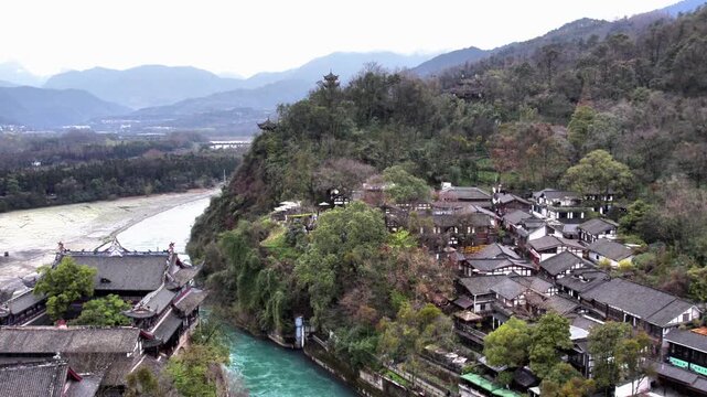 A historic water conservancy site lies by a winding river, with traditional buildings and forested mountains in the backdrop.