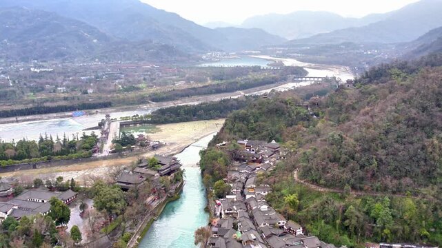 A high-angle shot shows a historic water conservancy project nestled between mountains and a flowing river, with traditional settlements nearby.