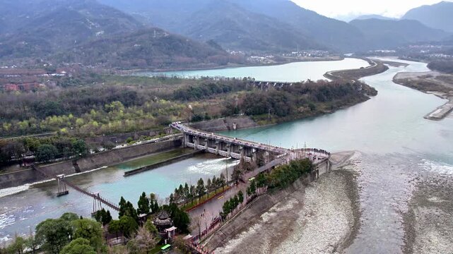 A hydraulic engineering structure diverts river flow, surrounded by mountains and vegetation, forming a scenic landscape.