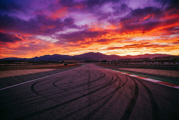 Fototapeta premium Dirt Road Winding Through Desert Landscape at Dramatic Sunset with Silhouetted Tracks