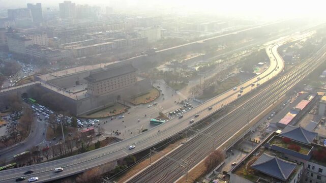 Aerial shot showing historic city gate adjacent to modern road and railway lines in hazy urban area.