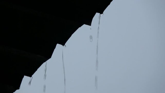 Heavy raindrops violently hitting and smashing onto a transparent corrugated plastic canopy roof at night, creating high splashes and water ripples against a dark background.
