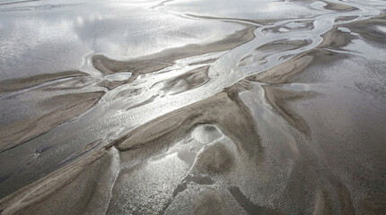 Obraz premium Glistening Low Tide Mudflats Reflect Dramatic Silver Sky Across Remote Coastal Wetland Landscape At Dawn
