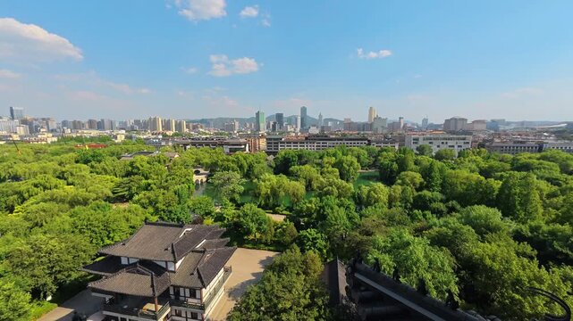 A high-angle view of a lush urban park with traditional buildings, set against a modern city skyline under a clear blue sky.