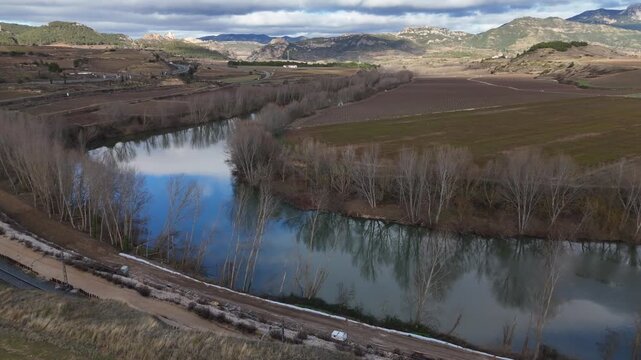 Aerial view of Ebro river reflecting a blue sky near winter vineyards and railway maintenance works in Haro, La Rioja, Spain