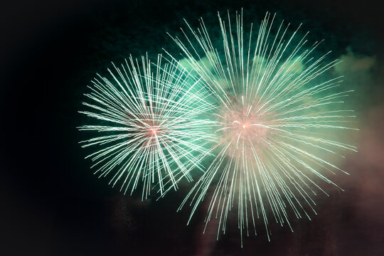 Vibrant multicolored fireworks explode in the dark night sky at a large scale festive event. Rich, bright flashes create an amazing spectacle