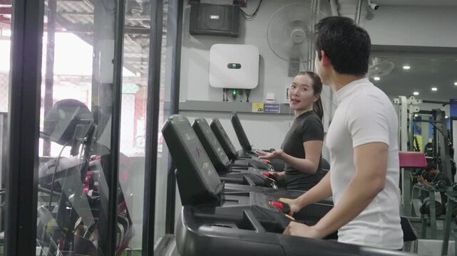 A friendly male trainer is setting up the treadmill display for an Asian woman exercising in a modern gym.