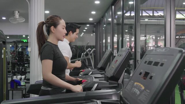 A friendly male trainer is setting up the treadmill display for an Asian woman exercising in a modern gym.