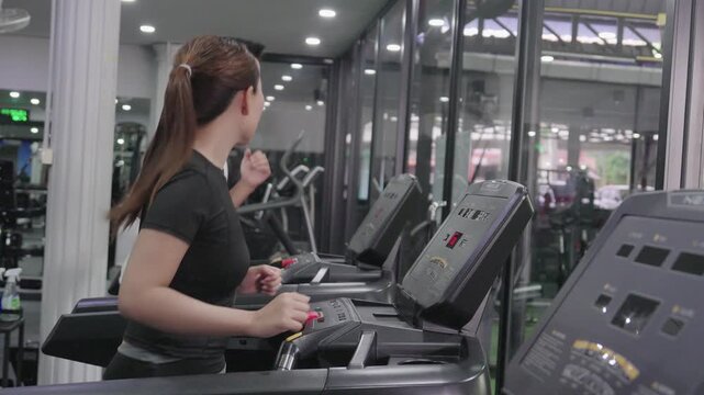 A friendly male trainer is setting up the treadmill display for an Asian woman exercising in a modern gym.