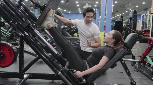Beautiful young Asian woman exercising on chest press machine with the help of her personal trainer at the gym.