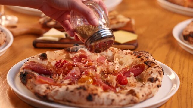 Hand Shaking Dried Oregano Seasoning Onto Fresh Gourmet Pizza
