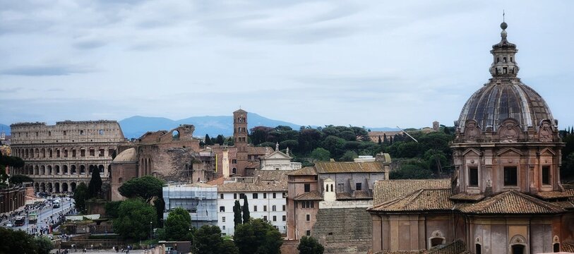 A view over the rooftops of Rome with the Colosseum church towers and a Baroque dome under a soft cloudy sky Italy.