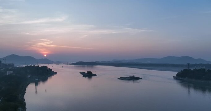 A stunning panning drone shot captures the Brahmaputra River at sunset, with golden reflections, serene waters, and majestic Assamese landscapes glowing in twilight. 4K
