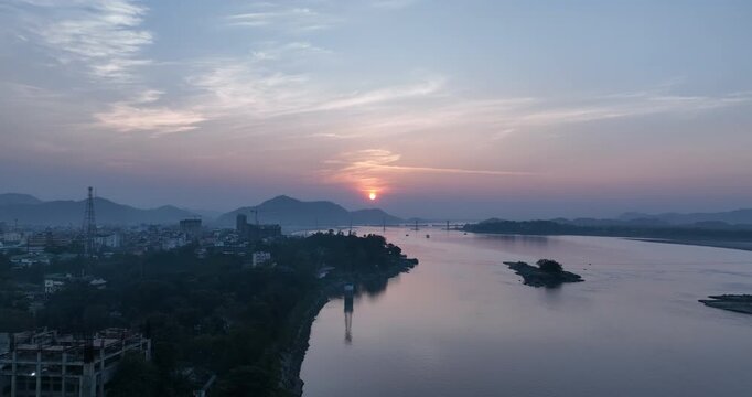 A drone shot during summer captures the Brahmaputra River beside Guwahati city at dusk, as the setting sun paints the sky with breath-taking golden hues. 4K
