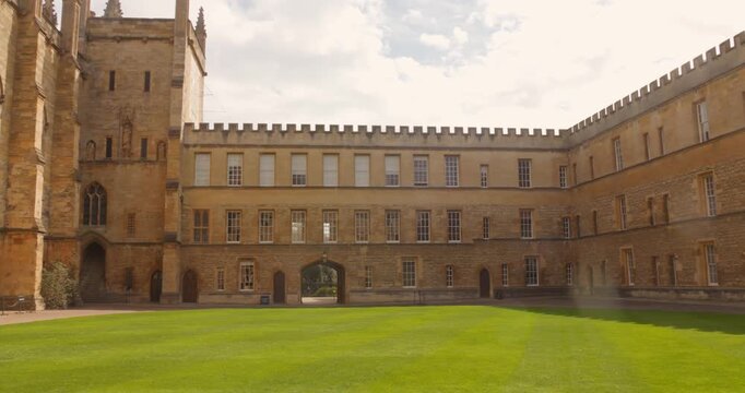 Camera glides across the green courtyard framed by the stone walls and arched passageway of New College at Oxford University.