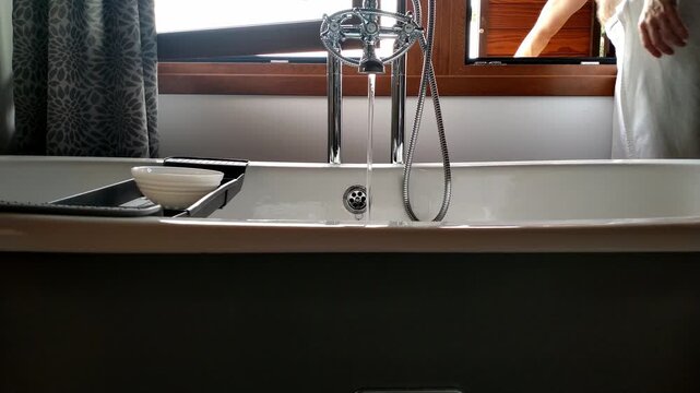 Person in towel opens window beside modern bathtub in bright bathroom interior