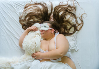 Curvy woman sleeping in white bed while wearing fluffy sleep mask and hugging plush toy creating a cozy bedtime scene with comfort relaxation and playful dreaming atmosphere. © ullision
