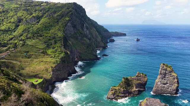 Cinematic rotating aerial footage revealing towering volcanic cliffs turquoise Atlantic waters and rugged sea stacks along the coast of Flores Island Azores Portugal