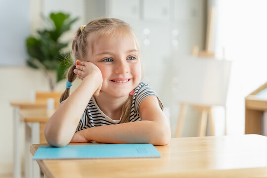 Young girl smiling at desk, Portrait of Smiling young girl sitting at classroom desk with notebook, Cute primary student studying in school, Happy elementary school girl smiling at desk in classroom