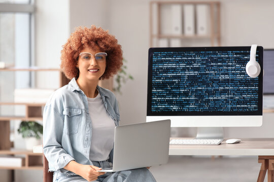 Young female programmer working with laptop and computer in office