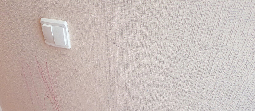 a light-colored wall covered in scribbles, wallpaper by the light switch, in need of repair