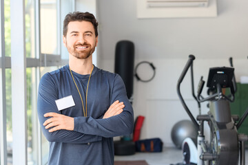 Fototapeta premium Smiling male fitness trainer standing with arms crossed in gym