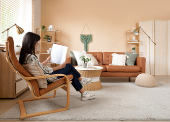 Young woman reading magazine in leather armchair at home
