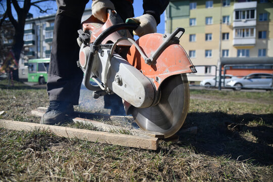 A worker cuts a wooden beam with a circular saw, construction work on a city street.