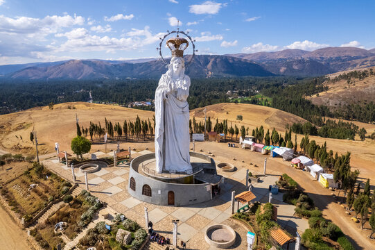 Aerial view of the large white statue of the Virgin of the Immaculate Conception, surrounded by a paved plaza, cypress trees, and arid mountainous landscape in Concepcion, Junin, Peru.