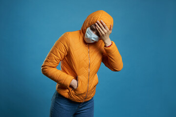 Fototapeta premium woman wearing hood in a protective face mask and coat over blue background. Model girl in medical mask and spring outfit, studio shot with copy space for your text. Anti-flu, anti-epidemic