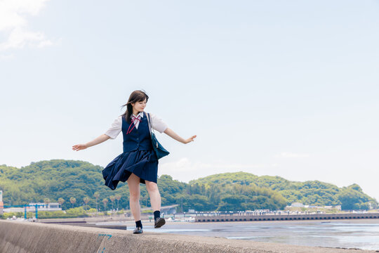 海辺の防波堤でバランスを取りながら歩く女子高校生