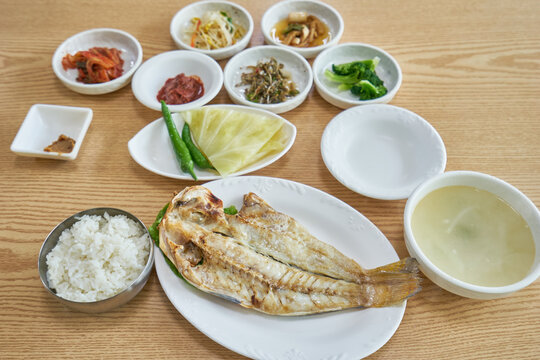 This authentic Korean Okdom-gui Baekban features a perfectly grilled, butterflied red tilefish on a wooden table. It is accompanied by white rice, clear soup, and various traditional side dishes.