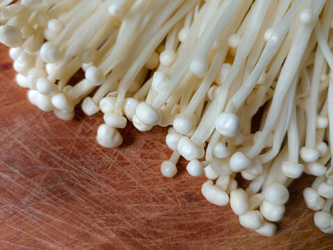 Fresh raw enoki mushrooms or golden needle mushrooms served on a wooden plate, ready to cook.