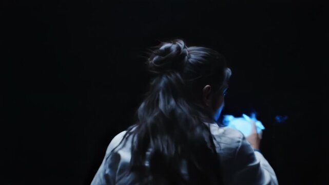 Young female scientist looking at a glowing blue orb in a dark laboratory setting