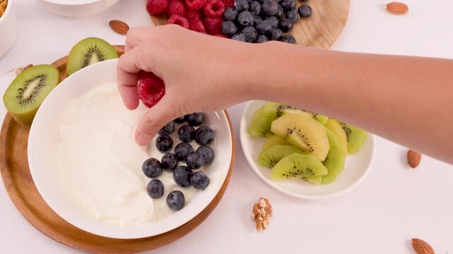 Hand Placing Fresh Raspberries into a Greek Yogurt Fruit Bowl