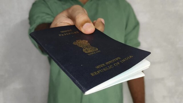 Closeup of Indian person hand showing or giving ordinary or general black colour passport towards camera to prove his nationality. International tour and travel identity concept.