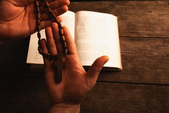 Man's hand holding a wooden cross on the bible.