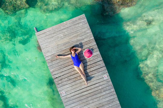 Aerial view of woman laying on wooden pier at sunny summer day in Cancun, Mexico, top view. Young sexy woman wearing bright swimsuit in summertime in Caribbean. Summer beach vacation concept
