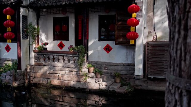 Red lanterns adorn a traditional building by the canal in Zhouzhuang, with stone steps leading to the water. Ideal for cultural documentaries or travel features.