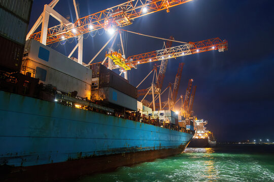 Container vessels docked in port at night, with cargo cranes towering above