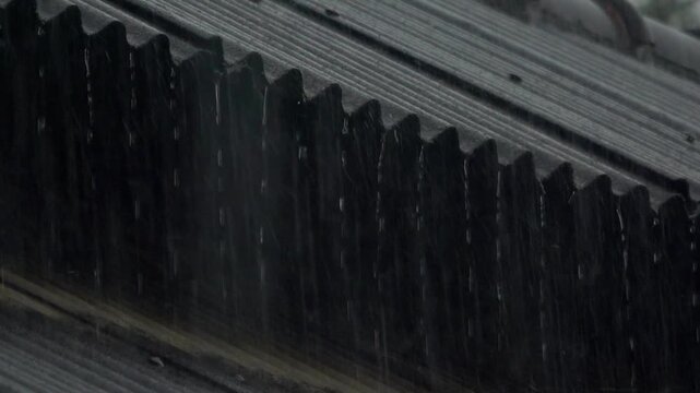 A close up slow motion shot of monsoon rain droplets sliding, clinging, and dripping off overhead electric utility wires during a heavy storm.
