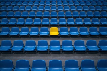 Naklejka premium A single yellow chair standing out in a large grid of empty blue stadium seats with difference individual distinction selection isolation highlight standout business leadership standing