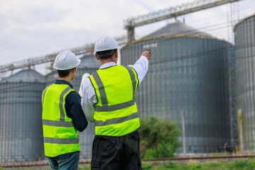 Engineers discussing plans pointing at grain silos at industrial facility © Crystal