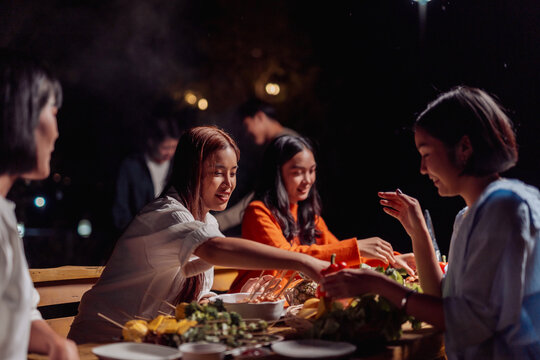 Friends enjoying barbecue dinner gathering at night outside